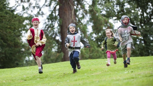 Four children in medieval dress running down a hill towards the camera, shouting